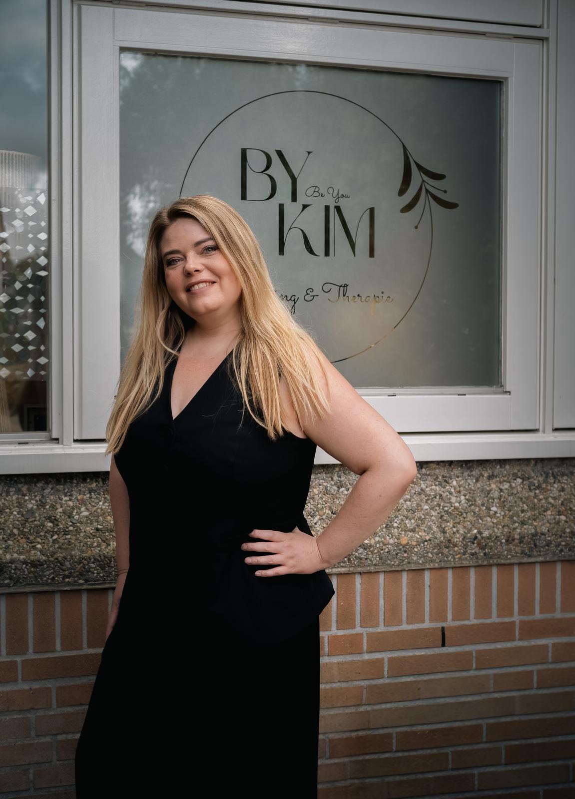 Glimlachende blonde vrouw houdt een wit document vast, close-up tegen donkere achtergrond met zachte belichting.